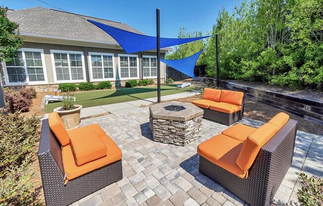 Outdoor cushioned chairs surrounding a fire pit on a cobblestone patio with a shaded grassy area