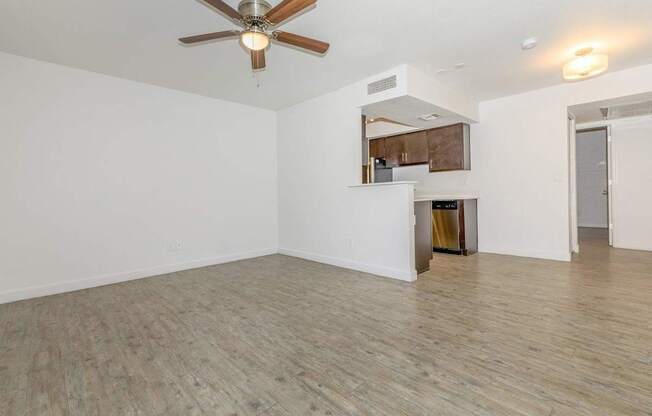A room with a ceiling fan and a kitchenette in the background.