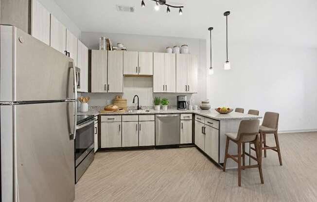 A kitchen with a refrigerator, oven, sink, and a chair.