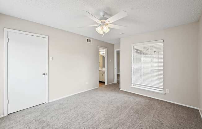 a bedroom with a ceiling fan and door to a bathroom