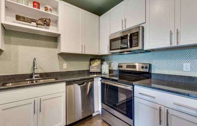 The Cleo - Spacious Kitchen with Wood-Style Flooring, Stylish Backsplash, Stainless Steel Appliances, and White Cabinetry