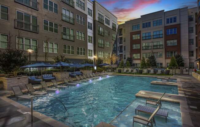 an apartment swimming pool with chairs and umbrellas at dusk
