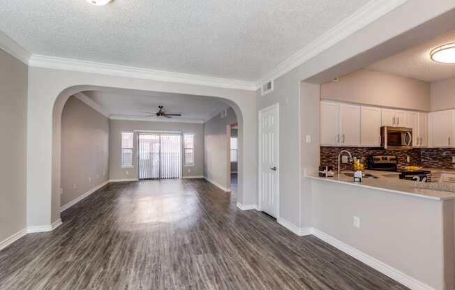 an empty living room with a kitchen and a ceiling fan