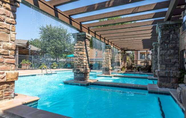 a resort style swimming pool with stone columns and a wooden canopy over it