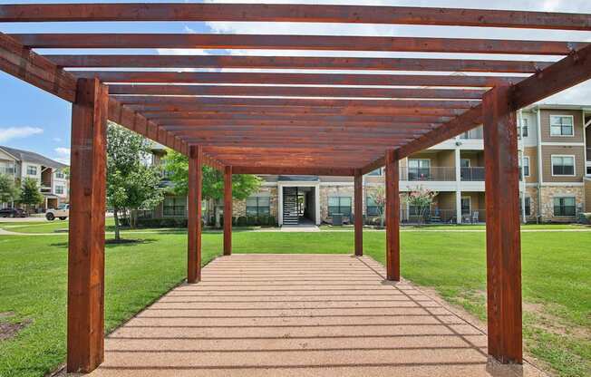 A wooden pergola over a brick walkway in a park.