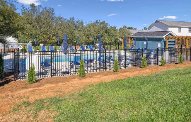 a fenced in pool with chairs and umbrellas in front of a house