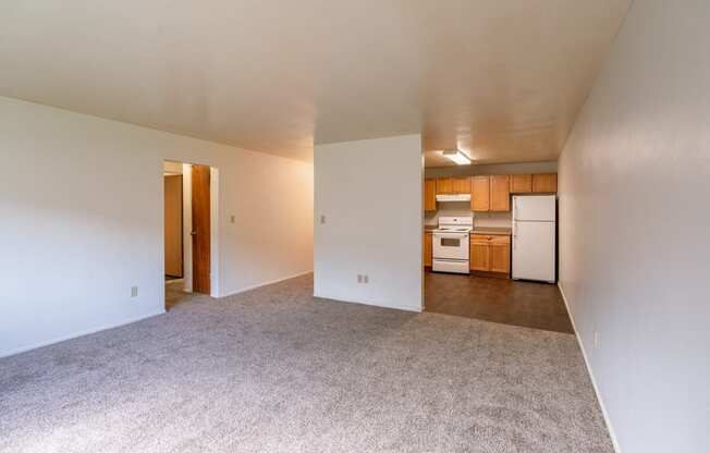 the living room and kitchen of an apartment with white walls and carpet. Fargo, ND Spring Apartments