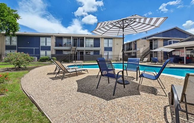 A sunny day at a poolside with chairs and an umbrella.