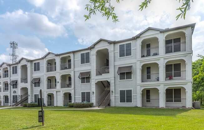 A large white apartment building with multiple balconies and a green lawn in front.