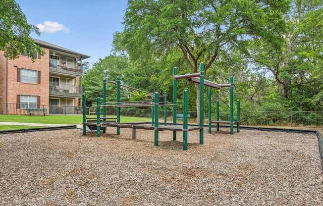 A playground with a green swing set and a brown gravel ground.