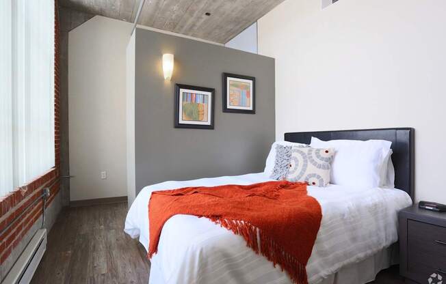 A bedroom with a bed covered in a white comforter and a red throw.