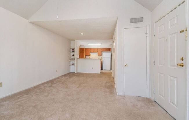 A white room with a door on the right and a kitchen area visible through the door.