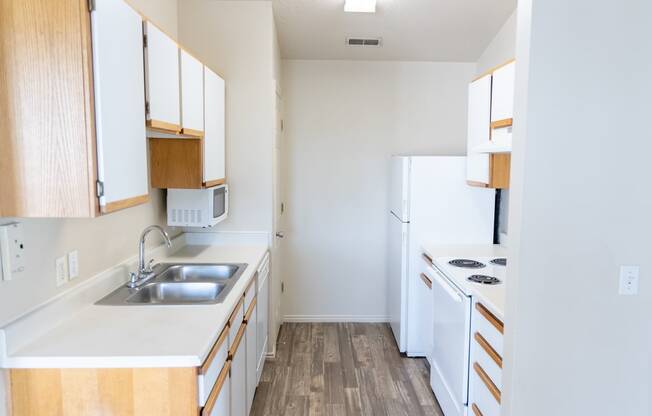 an empty kitchen with white appliances and wood flooring