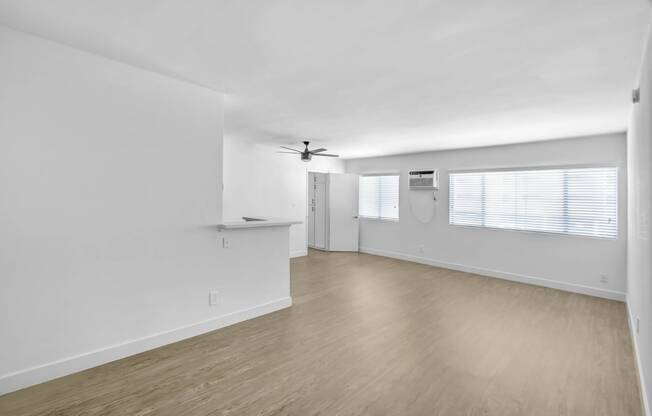 an empty living room with white walls and wood flooring and a ceiling fan