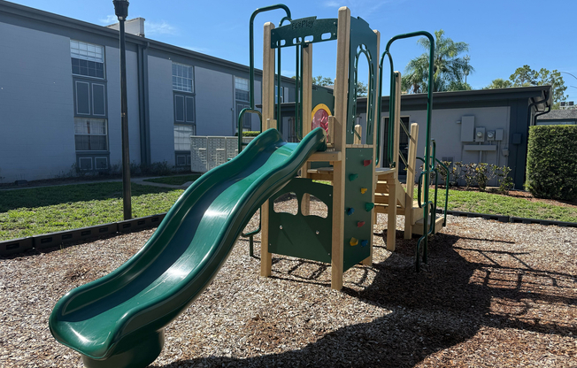 Inviting outdoor playground with a vibrant green slide and climbing area, perfect for children's play in a sunny apartment community.