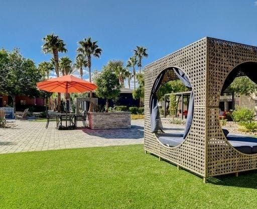 A modern outdoor seating area with a woven structure and a red umbrella.