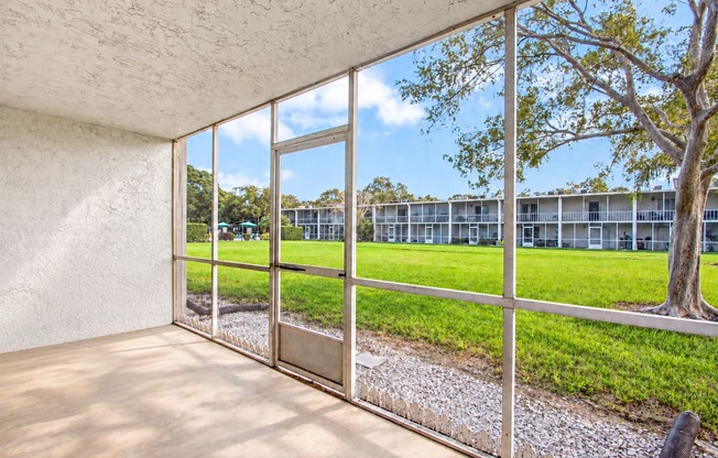 A room with a view of a grassy area and a building through the window.