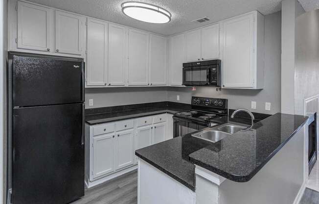 A black refrigerator is in a kitchen with white cabinets.