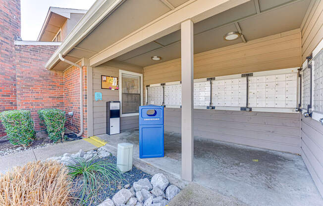 A blue recycling bin sits under a covered porch.