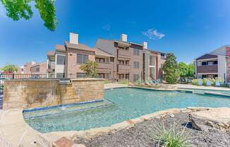 A large outdoor swimming pool surrounded by a stone wall and a grassy area.