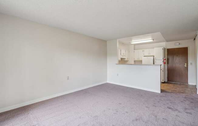 an empty living room with white walls and a kitchen