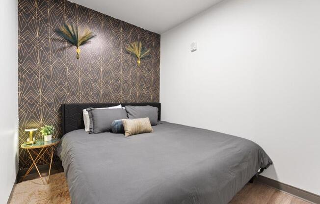 A bedroom with a grey bed and a wallpapered wall.