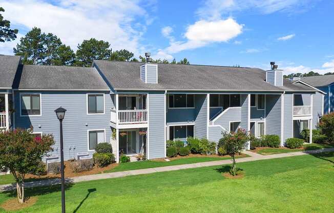 A large grey building with a balcony and a small garden in front.