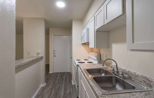 Kitchen with white cabinets and appliances in a 1 bedroom, 1 bath 752 sq ft apartment home with hardwoodlike flooring throughout at The Biltmore Apartments located in the Vickery Midtown neighborhood of Dallas, TX.