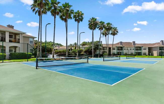 A tennis court surrounded by palm trees and apartment buildings.