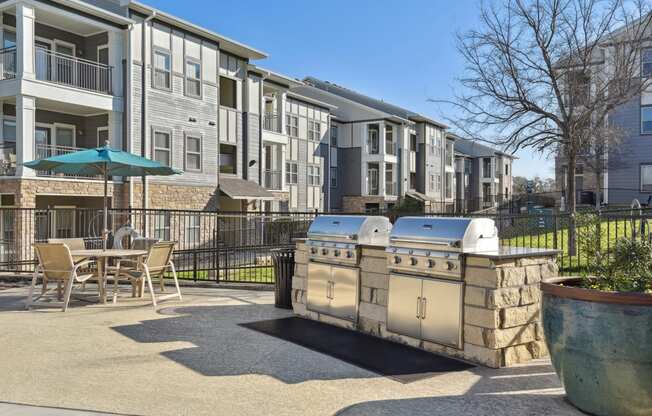 a patio with a grill and a table and chairs in front of an apartment building