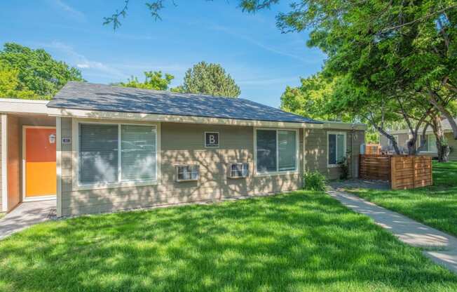 A Park View apartment home with an orange door and a yard with green grass, trees and a private patio.at Park View Apartments, Wenatchee, WA