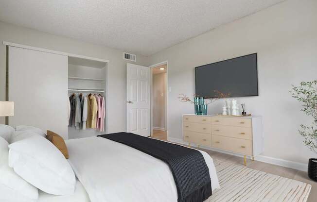 Aurora, CO Apartments – Aurora Meadows – A bedroom with a large bed, a dresser, and a flat-screen TV mounted on the wall.