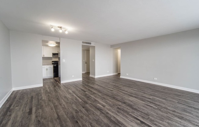 an empty living room with wood flooring and a kitchen