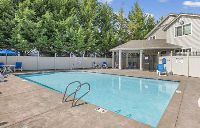 A swimming pool with a pavilion and blue lounge chairs surrounding it at Abbey Rowe Apartments in Olympia, WA