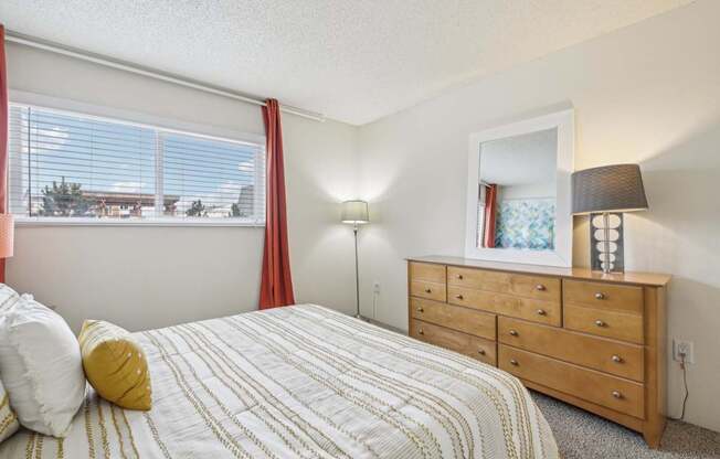 A bedroom with a bed, dresser, and window with red curtains.