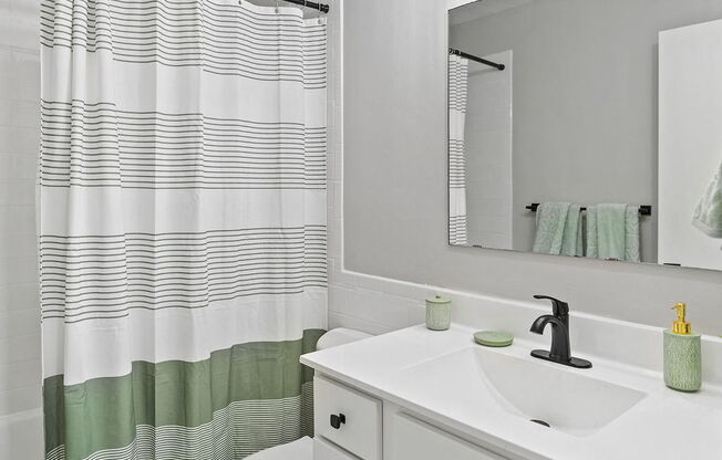 a white bathroom with a green and white striped shower curtain