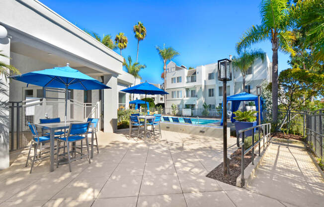 a patio with blue chairs and umbrellas and a swimming pool