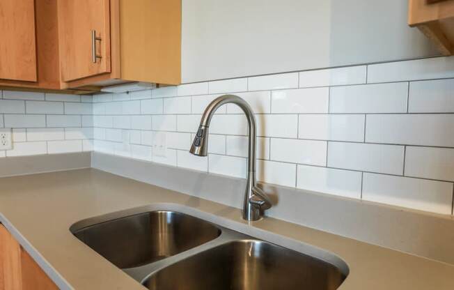 A kitchen sink with a chrome faucet and a white tile backsplash.