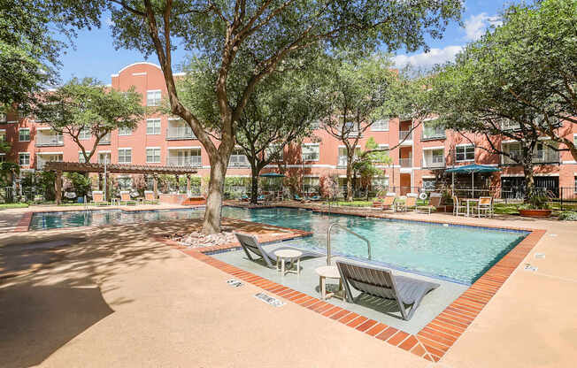 A pool surrounded by trees and chairs in front of a red building.