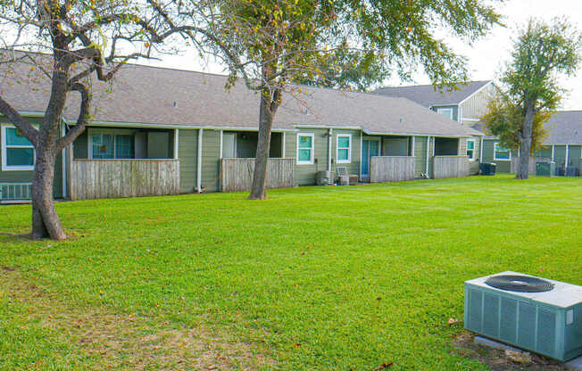 A grassy area in front of a building with a tree and a small air conditioning unit.