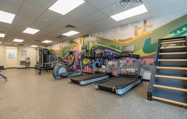 A gym with treadmills, weights, and a wall mural.
