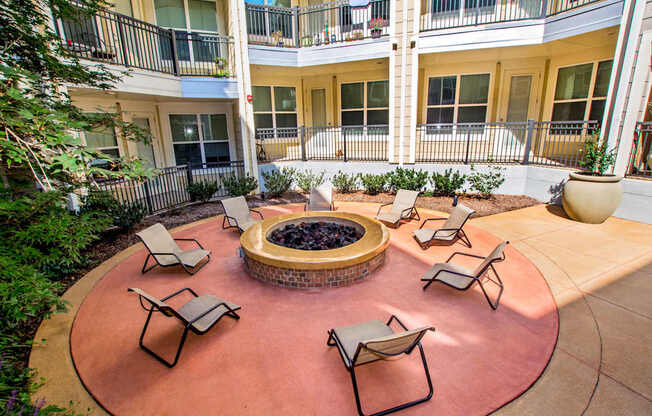 A patio with chairs and a fire pit in the middle of a courtyard.