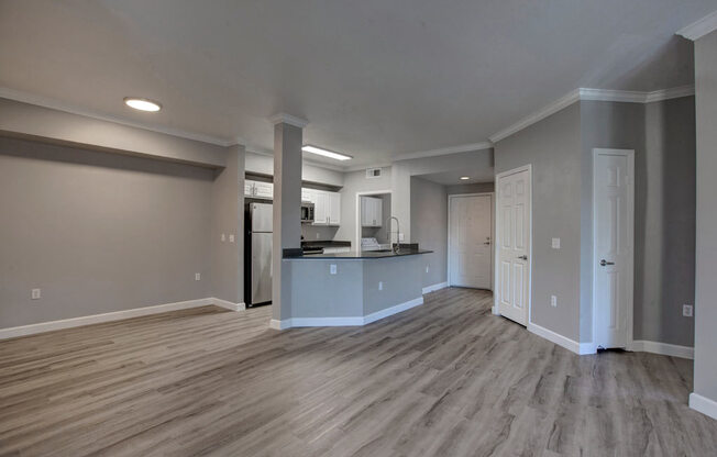an empty living room with a kitchen in the background