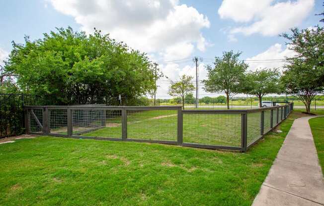 A fenced green field with trees and a cloudy sky.