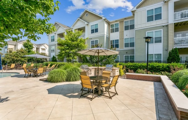 A patio with chairs and an umbrella in front of apartment buildings.at Century Hampton Roads, Virginia, 23435