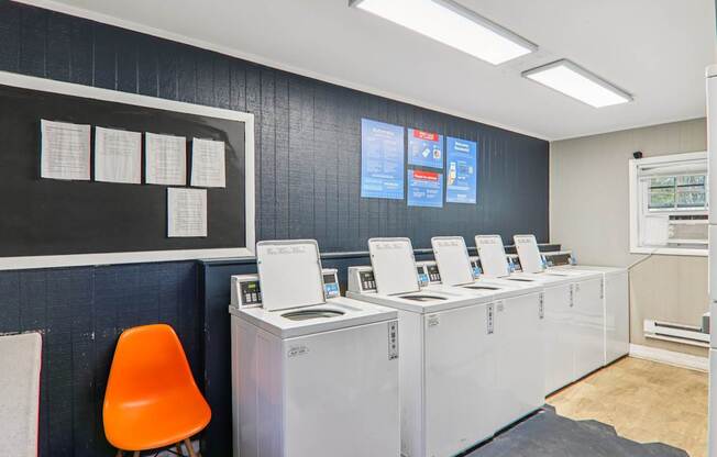 A room with a row of washing machines and a chair.