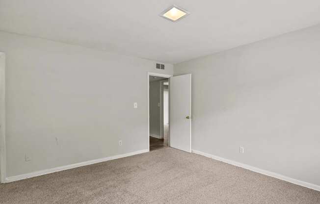 a bedroom with white walls and carpet and a door to a hallway