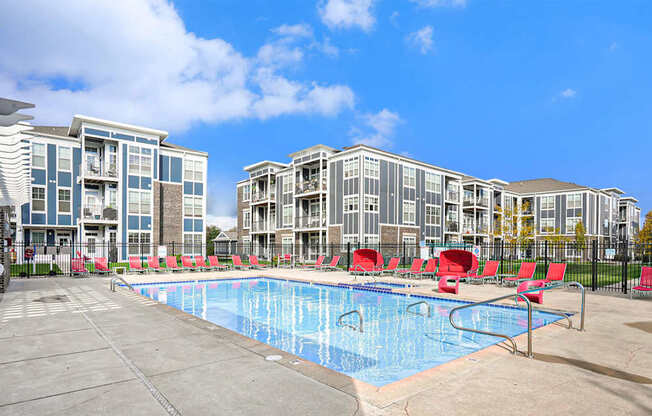 A swimming pool surrounded by red chairs and buildings in the background.
