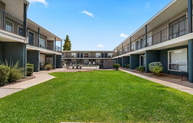 a grassy courtyard between two apartment buildings with a lawn