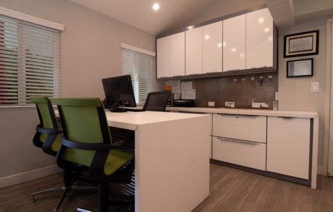 A white desk with a green chair in front of a white cabinet.